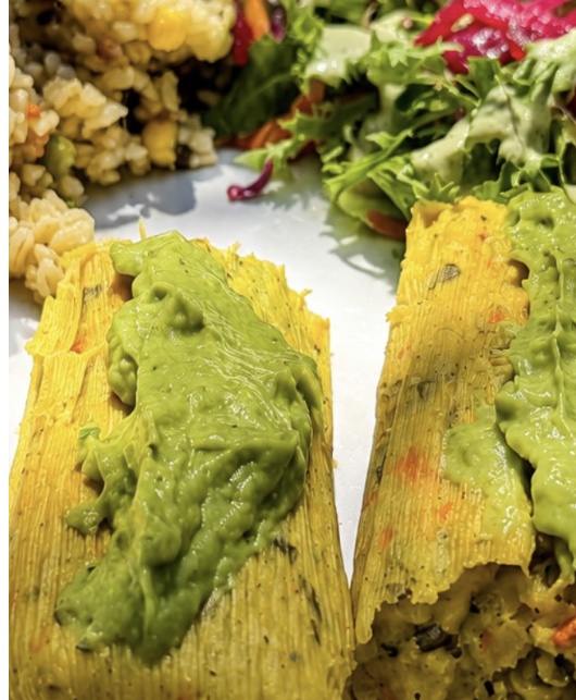 Two corn tamales topped with avocado sauce, beside cilantro brown rice and a fresh salad