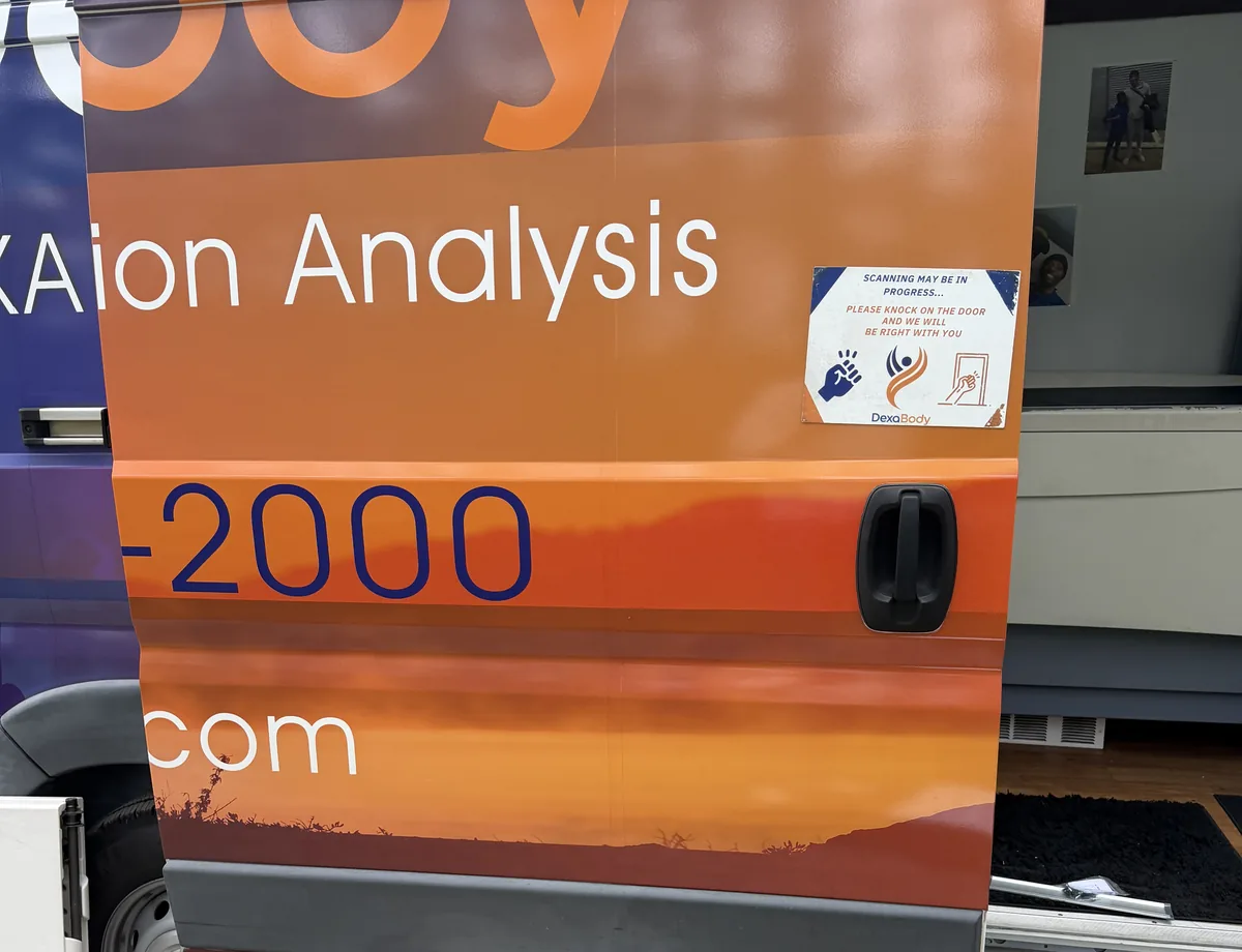 The open door of the Dexa Body van, with a sign asking guests to knock while scanning is in progress