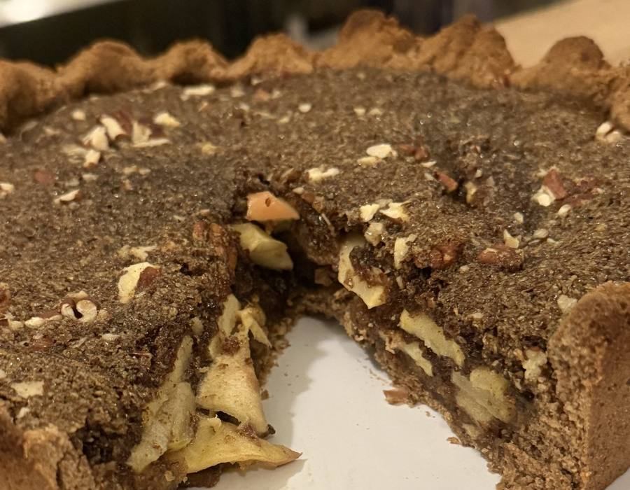 A whole apple pie with a slice removed, showing layers of real sliced apple beneath a nut crumble topping in a whole-food crust