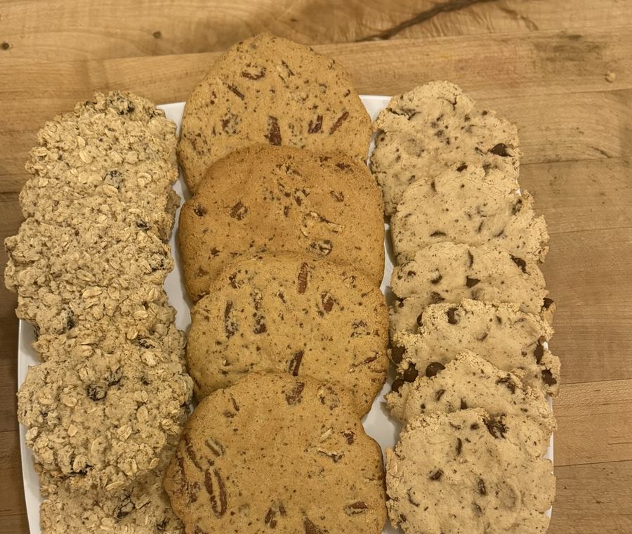 Three varieties of cookies laid out in three rows on a white platter: an oat cookie, a pecan cookie, and a chocolate chunk cookie