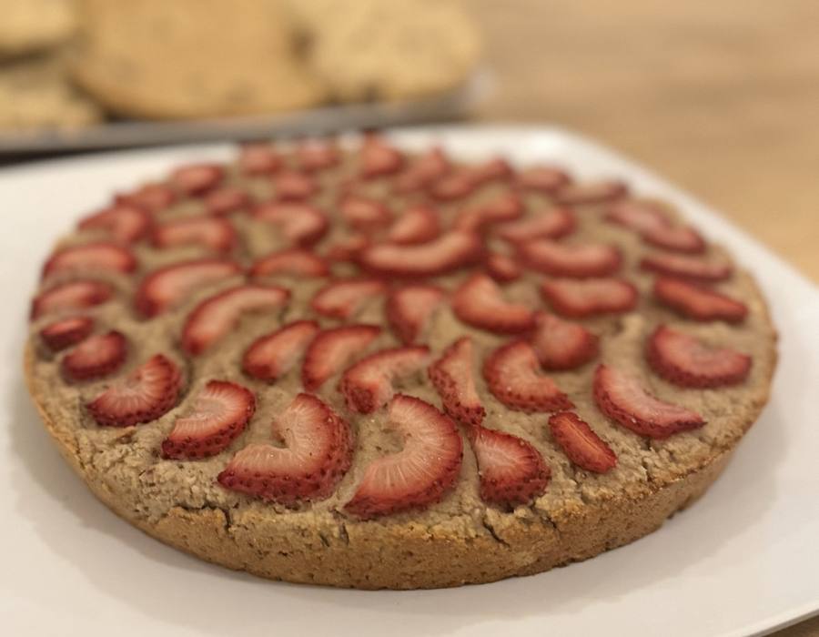 A whole strawberry cake on a white platter, the top covered edge to edge in a spiral of sliced fresh strawberries