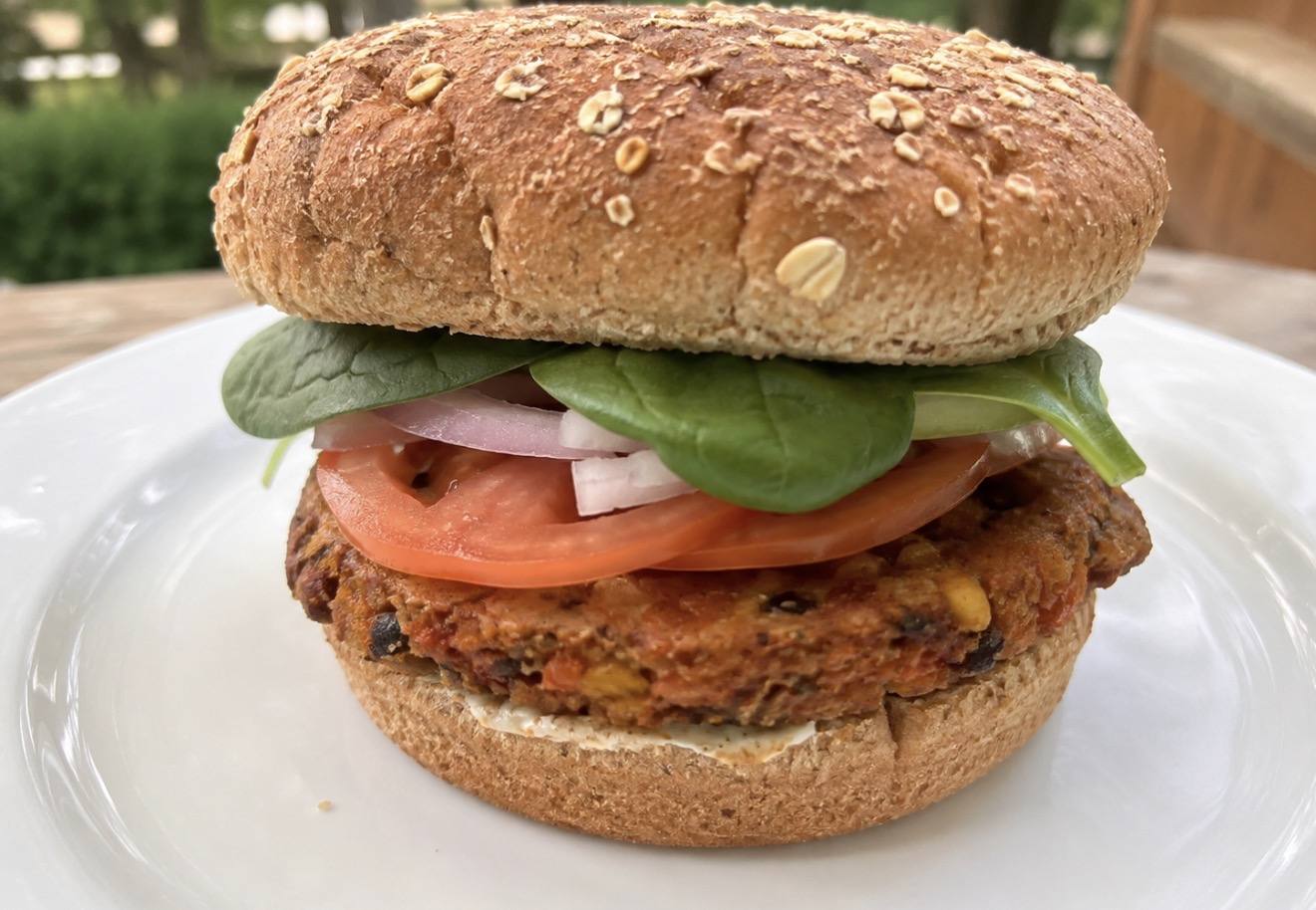 A whole-food plant-based baked burger on an Ezekiel bun with tomato, onion and spinach