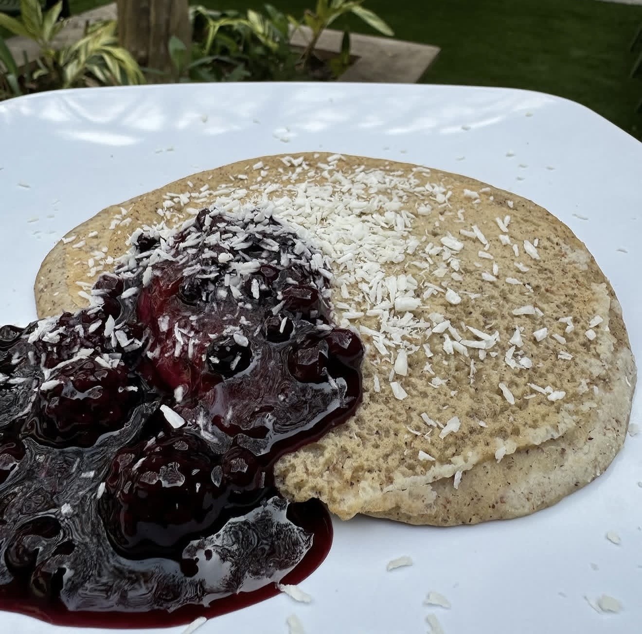 A whole-food pancake topped with warm blueberry compote and shredded coconut