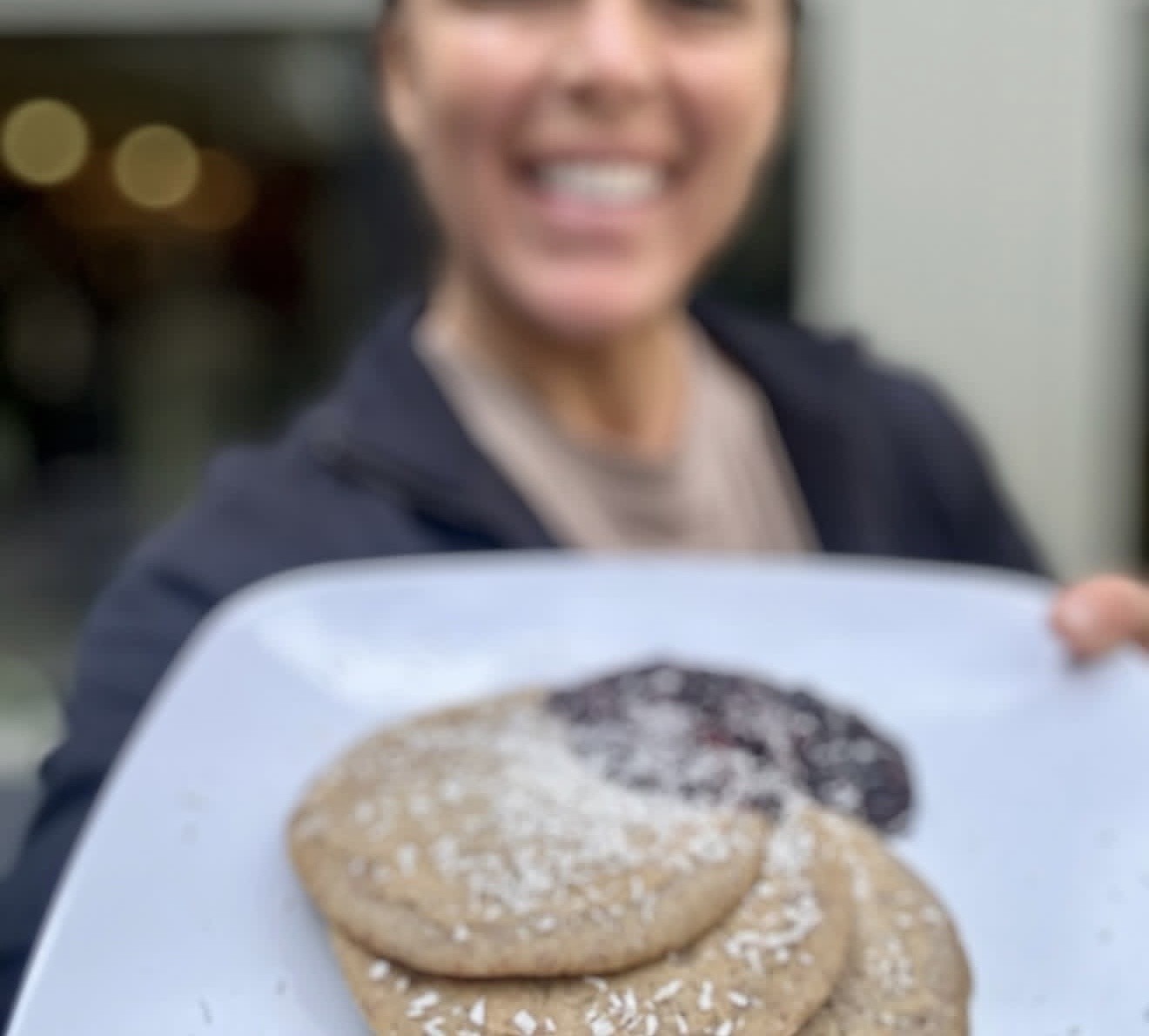 A guest smiling as she holds out a plate of pancakes with berry compote