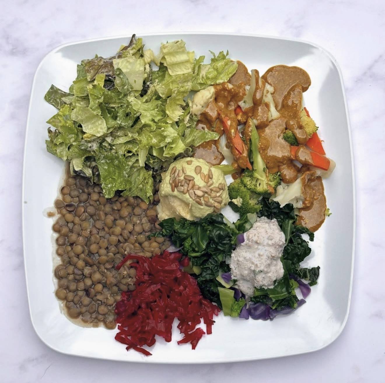 A plate of lentils, steamed greens, salad, shredded beet and cauliflower with a cashew sauce