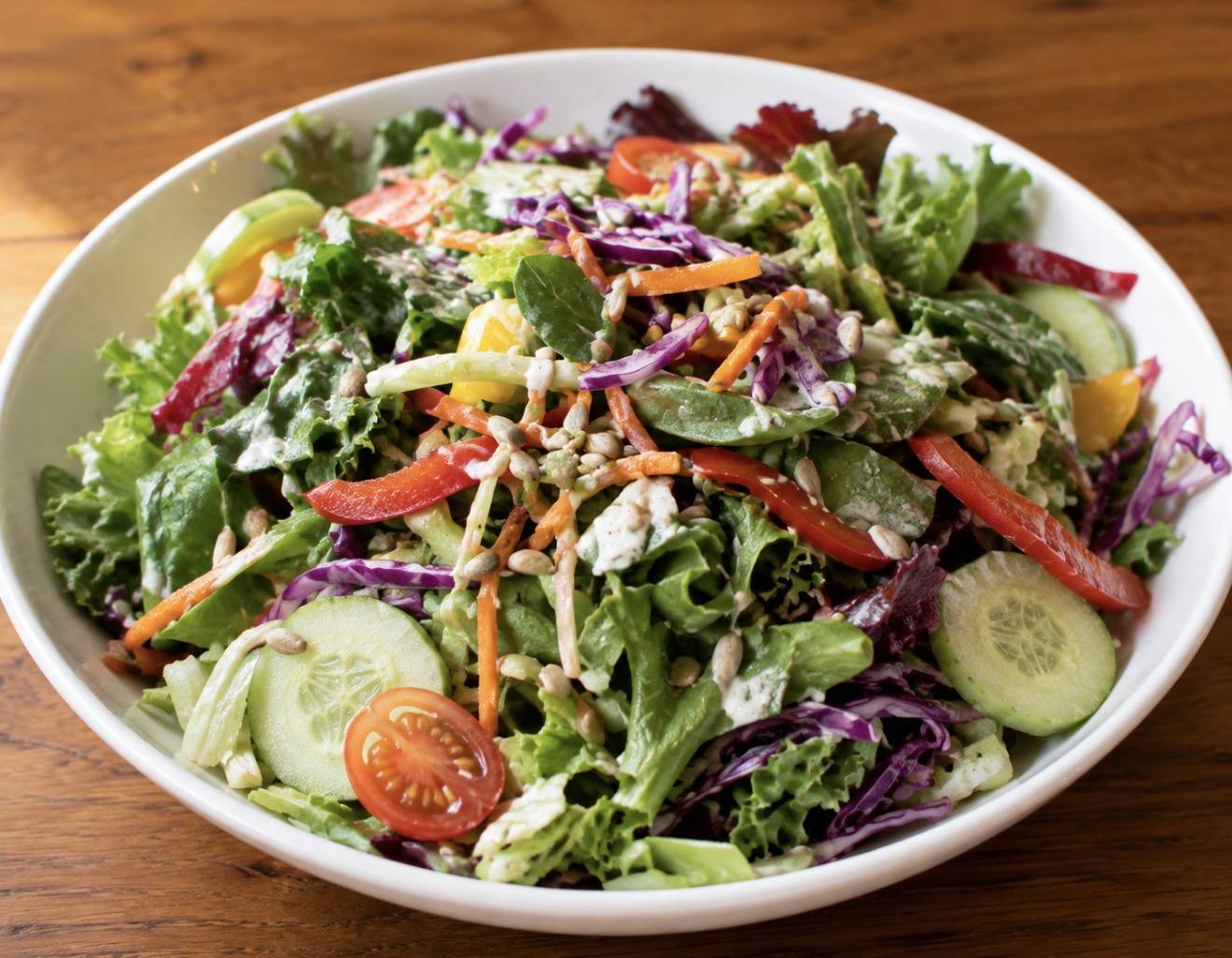 A bowl from the salad bar with mixed greens, tomato, cucumber, peppers, red cabbage and seeds