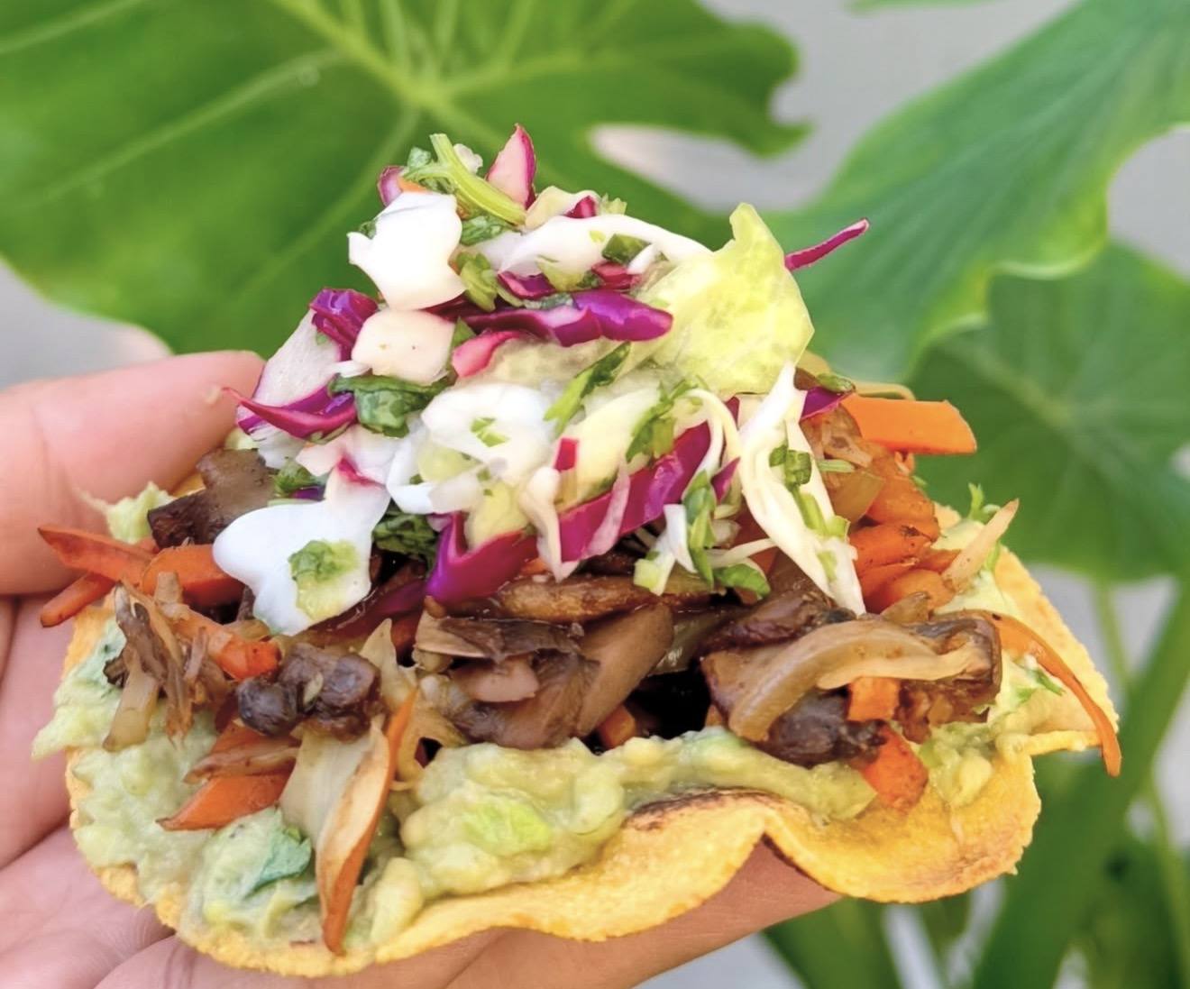 A heirloom corn tostada piled with guacamole, beans, grilled vegetables and slaw