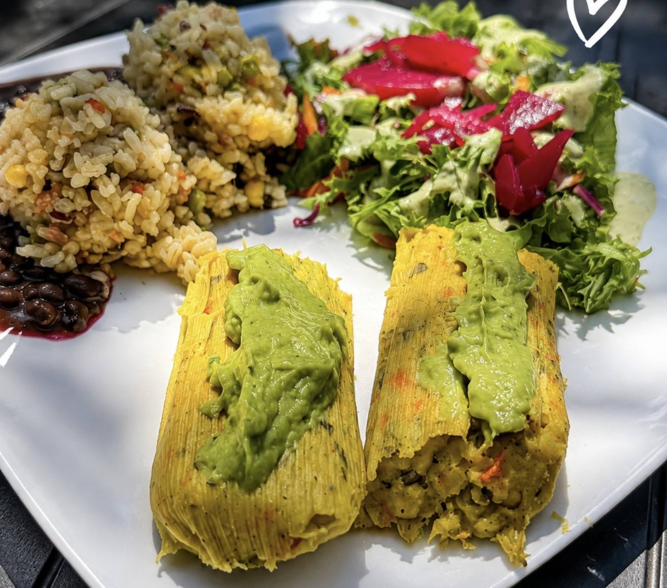 Two corn tamales topped with avocado sauce, served with rice and salad